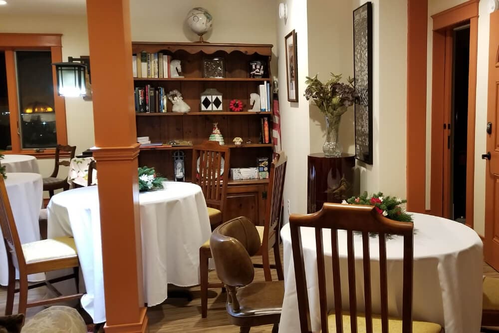 Cozy dining area with round tables, wooden chairs, and a bookshelf.